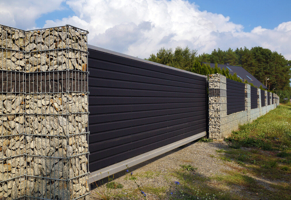 Duże ogrodzenie gabionowe z szarego pokruszonego wapienia z warstwą ciemnej skały na obwodzie ogrodzenia